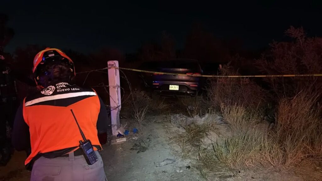 incendio-accidente-autopista-laredo - NL Directo Civil protection worker in an orange vest and helmet stands near a taped-off blue SUV at night.