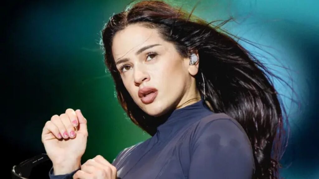 Female performer singing on stage with in-ear monitor, dark blue top, hair blowing in the lights.